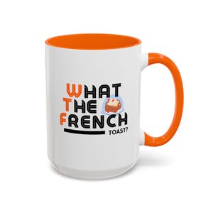 May include: White ceramic mug with an orange rim and handle. The mug features black text that reads "WHAT THE FRENCH TOAST?" with a cartoon image of French toast.
