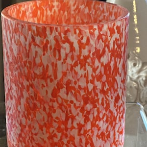 May include: A cylindrical glass candle holder with a white and orange speckled pattern. The holder is made of clear glass with a textured surface.