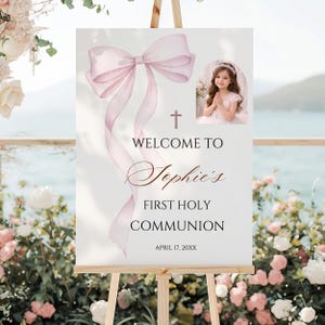 Puede incluir: Un letrero blanco sobre un caballete con un lazo y cintas de acuarela, una cruz y el texto "WELCOME TO Sophie's FIRST HOLY COMMUNION" con una foto de una niña. La fecha "APRIL 17, 20XX" está en la parte inferior.