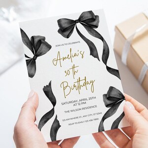 May include: A white invitation with black watercolor bows and gold text. The text reads "Join us to celebrate Amelia's 30th Birthday. Saturday, April 25th at 12 PM. The Wilson Residence. 123 Anywhere St, Any City, ST 12345. RSVP to Emily 123-456-7890."