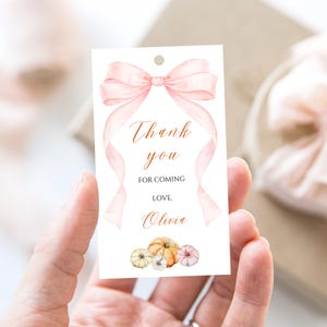 Può includere: Un'etichetta regalo bianca con un design ad acquerello. Presenta un fiocco rosa e nastri fluenti, con le parole "Thank you for coming, Love, Olivia" in elegante scrittura. Il fondo presenta zucche ad acquerello.