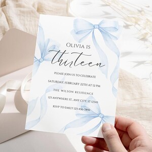 May include: A blue and white invitation card with a watercolor design of bows. The text on the card reads "Olivia is Thirteen. Please join us to celebrate Saturday, February 22th at 12 PM. The Wilson Residence 123 Anywhere St. Any City. ST 12345 RSVP to Emily 123-456-7890"