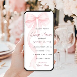 May include: A pink baby shower invitation on a smartphone screen with a watercolor bow design. The invitation reads "Please join us for a Baby Shower honoring Sophie Smith, Saturday, June 15th at 12 PM, Smith's Residence, 121 Anywhere St. Any City, ST 12345, RSVP to Emily 123-456-7890, Registered at Target & Amazon."