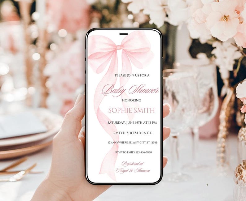 May include: A pink baby shower invitation on a smartphone screen with a watercolor bow design. The invitation reads "Please join us for a Baby Shower honoring Sophie Smith, Saturday, June 15th at 12 PM, Smith's Residence, 121 Anywhere St. Any City, ST 12345, RSVP to Emily 123-456-7890, Registered at Target & Amazon."