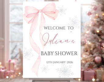 Könnte beinhalten: Ein weißes Schild mit rosa Schleife und Band-Design, mit den Worten "WELCOME TO Juliana BABY SHOWER 12TH JANUARY 2026" in rosa Schrift. Das Schild ist mit silbernen Schneeflocken verziert, passend für eine Babyparty.