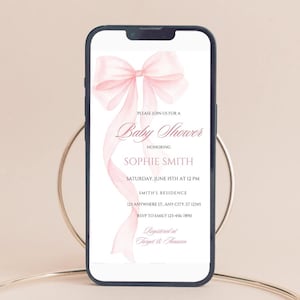 May include: A pink baby shower invitation with a watercolor bow on a white background. The invitation text reads "Please join us for a Baby Shower honoring Sophie Smith, Saturday, June 15th at 12 PM, Smith's Residence, 123 Anywhere St. Any City, ST 12345, RSVP to Emily 123-456-7890, Registered at Target & Amazon."