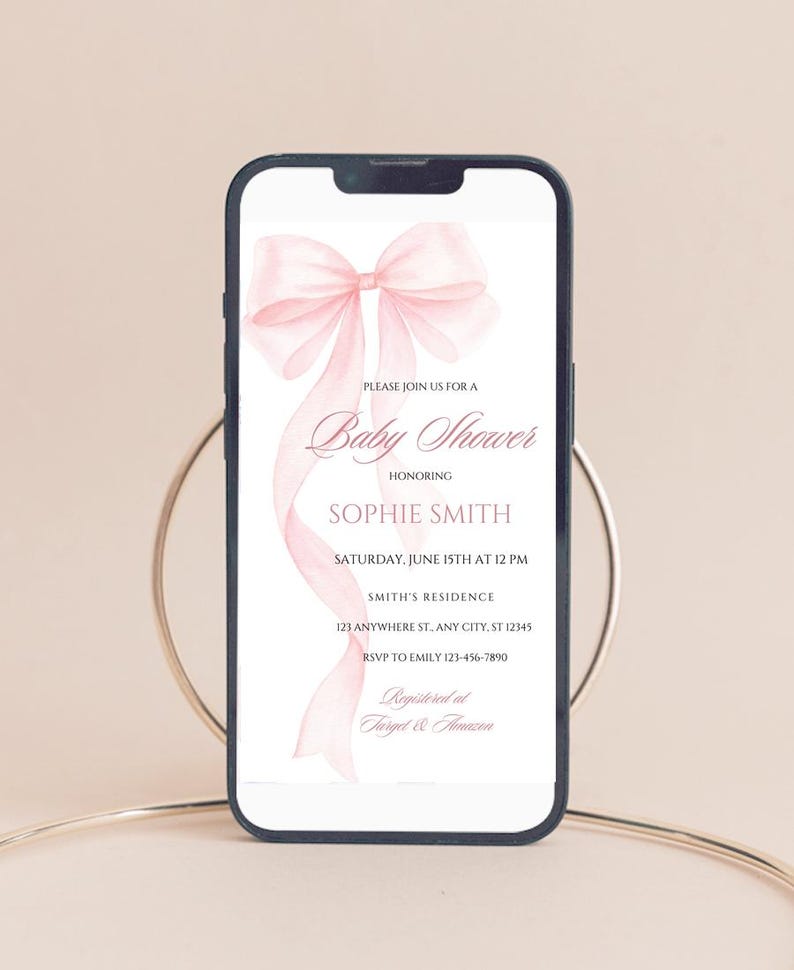May include: A pink baby shower invitation with a watercolor bow on a white background. The invitation text reads "Please join us for a Baby Shower honoring Sophie Smith, Saturday, June 15th at 12 PM, Smith's Residence, 123 Anywhere St. Any City, ST 12345, RSVP to Emily 123-456-7890, Registered at Target & Amazon."
