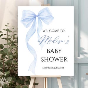May include: A blue watercolor bow with a white background. The text "Welcome to Madison's Baby Shower" is printed below the bow. The date "Saturday, June 21th" is printed below the text.