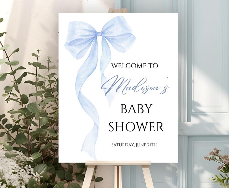 May include: A blue watercolor bow with a white background. The text "Welcome to Madison's Baby Shower" is printed below the bow. The date "Saturday, June 21th" is printed below the text.
