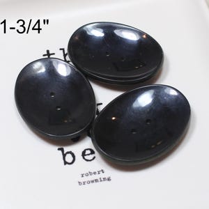 May include: Three smooth, glossy black oval buttons, each featuring two central holes. The buttons are arranged in a cluster, and the text 1-3/4" is visible, indicating their size. The buttons have a reflective surface and a simple, functional design.