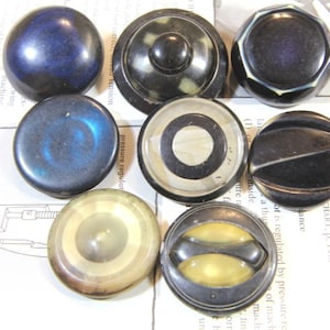 May include: Assortment of 10 vintage black and white plastic buttons with various designs. The buttons are round, oval, and octagonal in shape. Some buttons have a swirl pattern, while others have a concentric circle design.