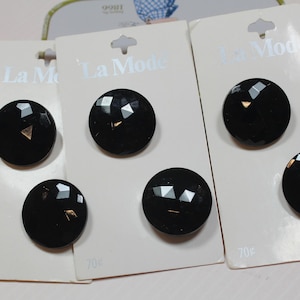 May include: Close-up of several black faceted buttons on white cards. The buttons have a geometric design and a gold-colored accent. The cards are labeled "La Mode" and have a price of 70¢.