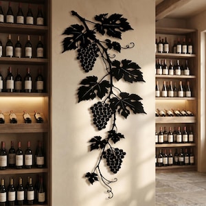 Op de afbeelding: Een zwart metalen wanddecoratie met een druivenrankontwerp, bestaande uit drie trossen druiven en diverse gedetailleerde bladeren. Het kunstwerk is verticaal bevestigd op een lichte muur tussen twee houten schappen vol met wijnflessen.