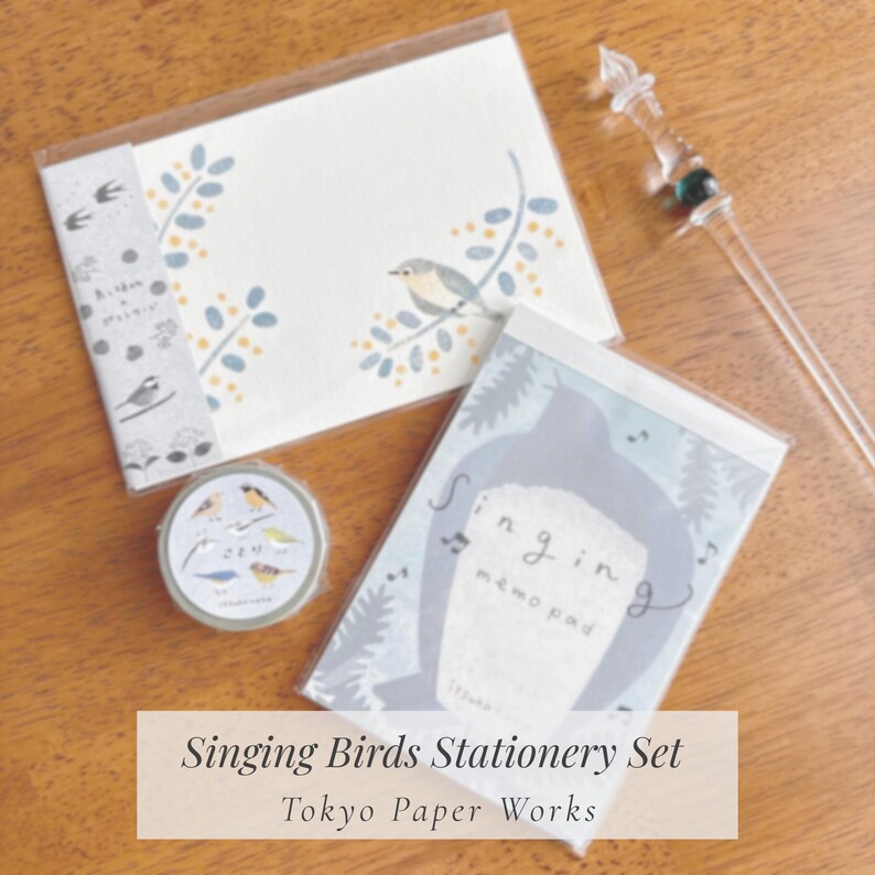 May include: A stationery set featuring a notepad, a roll of washi tape, and a notepad with bird illustrations. The set includes a notepad with a bird perched on a branch, and a roll of washi tape with various bird designs. The text "Singing Birds Stationery Set" is visible.