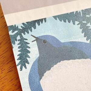 May include: A close-up of a printed illustration featuring a bluebird with a white chest, singing. The bird is set against a light blue background with a stylized tree branch. The top of the print has a light purple and white border.