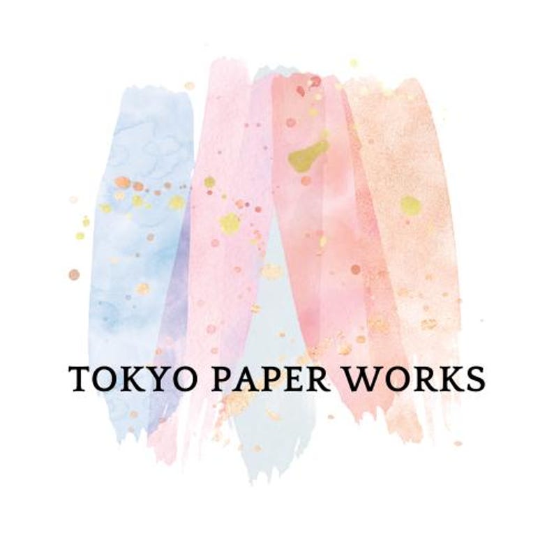 May include: Logo for Tokyo Paper Works. The design features watercolor brushstrokes in shades of blue, pink, and peach, with gold accents. The text "TOKYO PAPER WORKS" is displayed in a simple, black font below the brushstrokes.