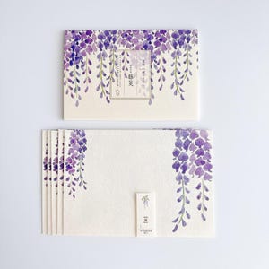 Op de afbeelding: Briefpapier set met een aquarelontwerp van paarse blauweregenbloemen. De set bevat een bijpassende envelop en verschillende notecards. Het ontwerp wordt herhaald op de envelop en de bovenkant van de notecards. Het briefpapier heeft Japanse tekst.