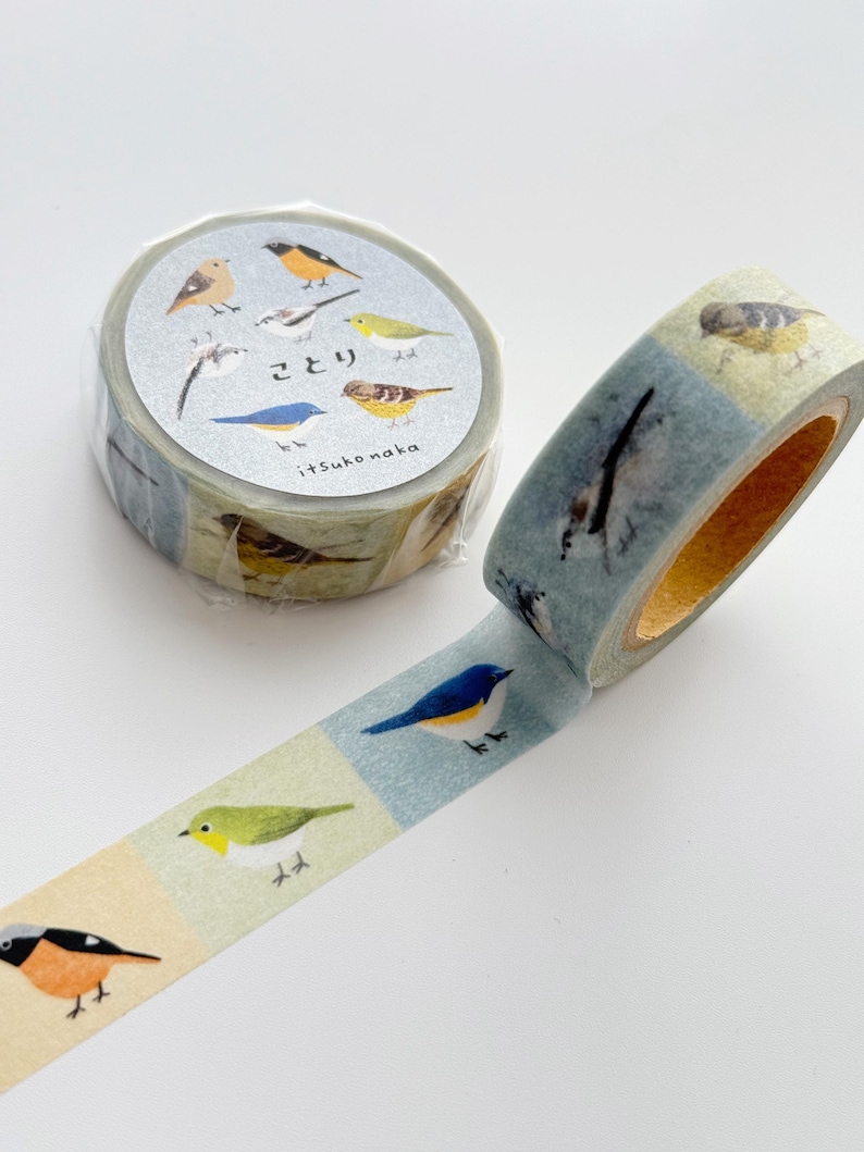 May include: Decorative washi tape featuring colorful bird illustrations. The tape roll is wrapped in clear plastic, with the tape itself displaying various bird species on a light blue and beige background. The tape is unrolled, showcasing the repeating bird pattern.