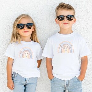 May include: Two children wearing white t-shirts with a rainbow graphic and the text "you are my everything" and "mini". The children are wearing sunglasses and blue jeans.