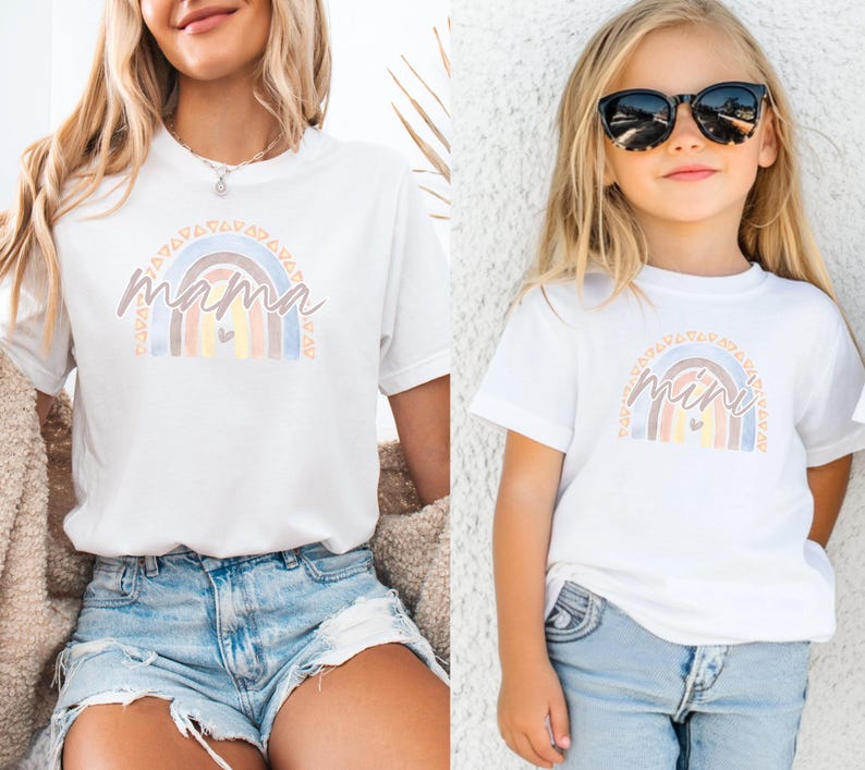 May include: Two white t-shirts with a rainbow design. The larger shirt says "mama" and the smaller shirt says "mini".