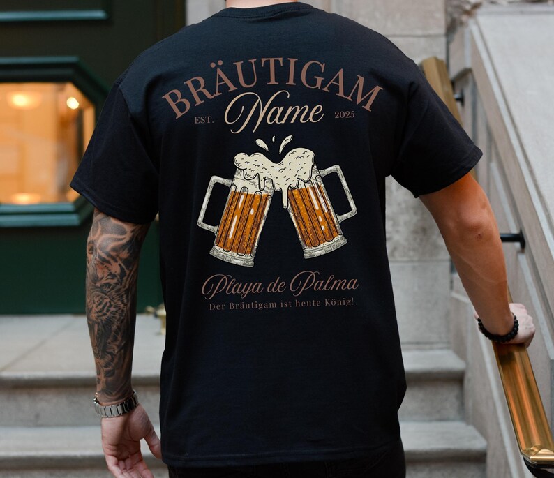 Puede incluir: Camiseta negra con un dise&ntilde;o de tem&aacute;tica cervecera. El dise&ntilde;o presenta dos jarras de cerveza chocando, con las palabras "BR&Auml;UTIGAM Name EST. 2025" y "Playa de Palma" impresas encima y debajo de las jarras. Tambi&eacute;n incluye la frase "Der Br&auml;utigam ist heute K&ouml;nig!"