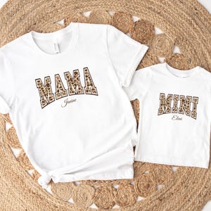 May include: White t-shirts with a leopard print design. The larger shirt says "MAMA Janine" and the smaller shirt says "MINI Eleni".