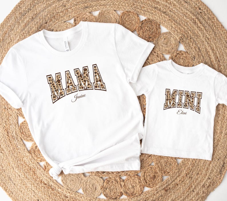May include: White t-shirts with a leopard print design. The larger shirt says "MAMA Janine" and the smaller shirt says "MINI Eleni".