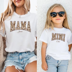 May include: White t-shirts with a leopard print design. The larger shirt says "MAMA Janine" and the smaller shirt says "MINI Eleni".