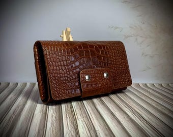 May include: A brown leather clutch with a crocodile embossed pattern. The clutch has a flap closure with two silver snaps.