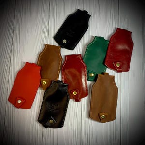 Puede incluir: Ocho llaveros de cuero en varios colores, incluyendo negro, marrón, rojo y verde. Cada llavero tiene un lazo de metal dorado.