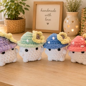 May include: Four small, handmade crochet mushroom figures with white bodies and rounded caps in lavender, mint green, blue, and pink. Each cap features white polka dots and a yellow sunflower accent. The figures have black bead eyes and small limbs.