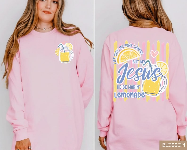 May include: A light pink long-sleeve shirt with a lemonade graphic on the front and back. The front features a yellow lemonade jar with lemons. The back has the text "Life gave me some lemons but my Jesus he be makin' lemonade."