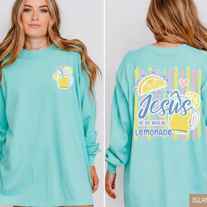 May include: A light turquoise long-sleeve shirt with a lemonade graphic on the front and back. The front features a lemonade glass with lemons and a straw. The back has the text "Life gave me some lemons but my Jesus he be makin' lemonade."