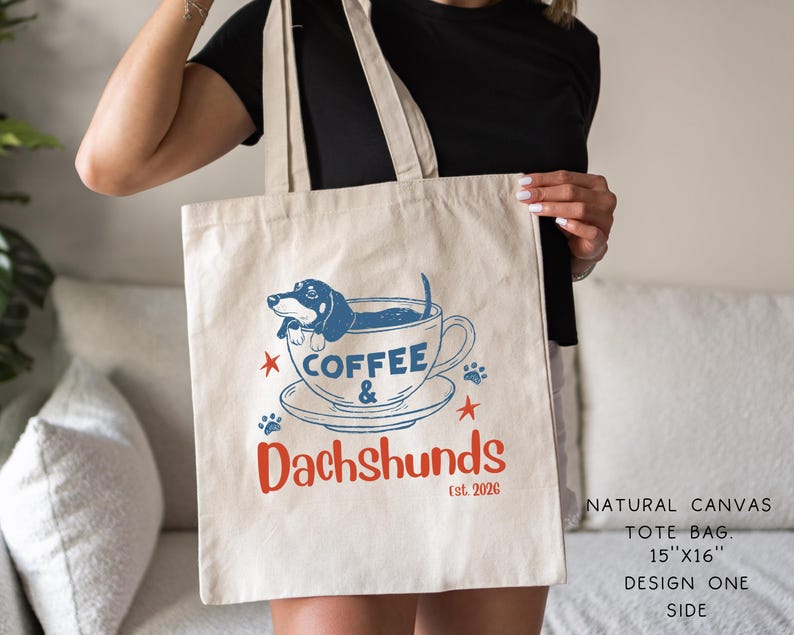 Peut inclure: Un sac fourre-tout en toile de couleur naturelle avec un motif bleu et rouge. Le motif repr&eacute;sente un teckel dans une tasse &agrave; caf&eacute;, avec les mots "Coffee & Dachshunds" et "Est. 2026". Le sac mesure 38 cm x 41 cm.