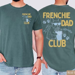 May include: A blue spruce t-shirt with "FRENCHIE DAD CLUB" printed on the front and back. The back features a French Bulldog wearing sunglasses, drinking from a cup, and the text "life is better with frenchies."