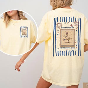 May include: Pale yellow t-shirt with a patriotic goose design. The back displays a framed illustration of a goose in a top hat, with the text "250th Anniversary" and "Just a Patriotic Goose". The front has a smaller version of the graphic.