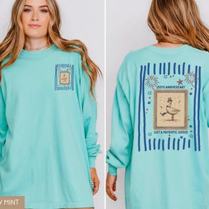 May include: A long-sleeved, chalky mint-coloured shirt with a graphic on the front and back. The front graphic is a framed goose. The back graphic says "250th Anniversary" and "Just a Patriotic Goose" with fireworks and stars.