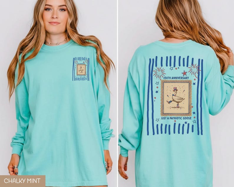 May include: A long-sleeved, chalky mint-coloured shirt with a graphic on the front and back. The front graphic is a framed goose. The back graphic says "250th Anniversary" and "Just a Patriotic Goose" with fireworks and stars.