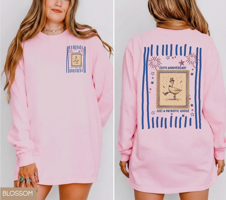 May include: A pale pink long-sleeved top featuring a goose in a hat graphic, with the text "Just a Patriotic Goose" and "250th Anniversary". The design is framed by blue stripes and stars.
