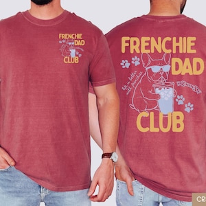 May include: Crimson t-shirt with "FRENCHIE DAD CLUB" text and a French Bulldog graphic. The front features a small design, while the back showcases a larger illustration of the dog with sunglasses, a drink, and paw prints.