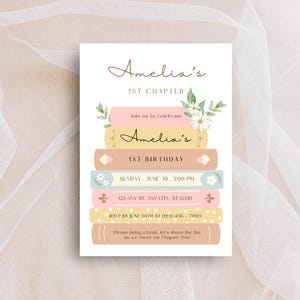 Pode incluir: Um convite de aniversário de pilha de livros rosa e amarelo com um design floral. O convite diz "Amelia's 1st Chapter" e "Join us to celebrate Amelia's 1st Birthday". O convite também inclui a data, a hora e o local da festa. As informações de RSVP estão incluídas na parte inferior do convite.