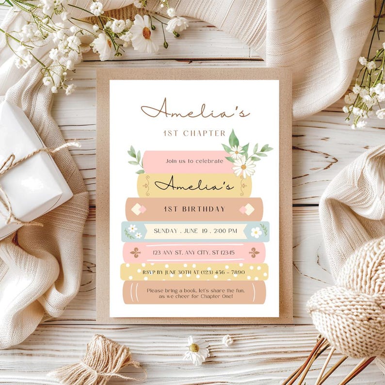 Op de afbeelding: Een roze en gele uitnodiging met een stapel boeken versierd met bloemen en de tekst "Amelia's 1st Chapter" en "Amelia's 1st Birthday". De uitnodiging bevat de datum, tijd, adres en RSVP-informatie.