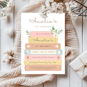 Op de afbeelding: Een roze en blauwe uitnodiging met een stapel boeken versierd met bloemen. De uitnodiging luidt "Amelia's 1st Chapter" en "Amelia's 1st Birthday". De uitnodiging bevat de datum, tijd en het adres voor het evenement. Het bevat ook een RSVP-verzoek en een verzoek om een boek mee te nemen.