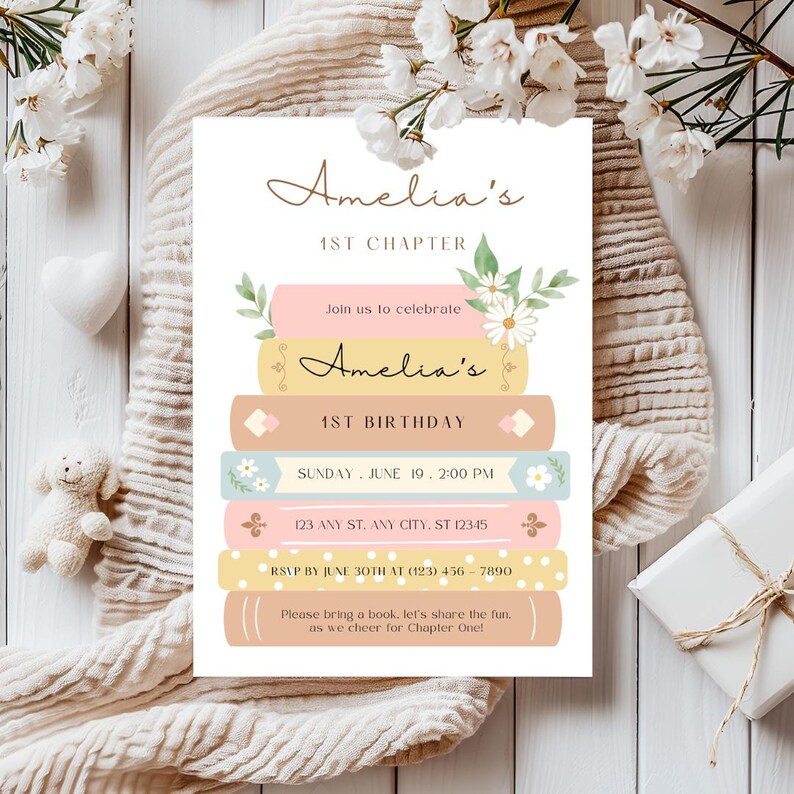Op de afbeelding: Een roze en blauwe uitnodiging met een stapel boeken versierd met bloemen. De uitnodiging luidt "Amelia's 1st Chapter" en "Amelia's 1st Birthday". De uitnodiging bevat de datum, tijd en het adres voor het evenement. Het bevat ook een RSVP-verzoek en een verzoek om een boek mee te nemen.