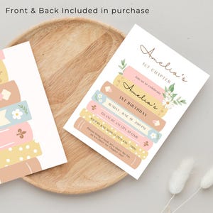 Op de afbeelding: Een afdrukbare uitnodiging voor een eerste verjaardagsfeest met een boekthema. De uitnodiging toont een stapel kleurrijke boeken met bloemen en de tekst "Amelia's 1st Chapter" en "Amelia's 1st Birthday".