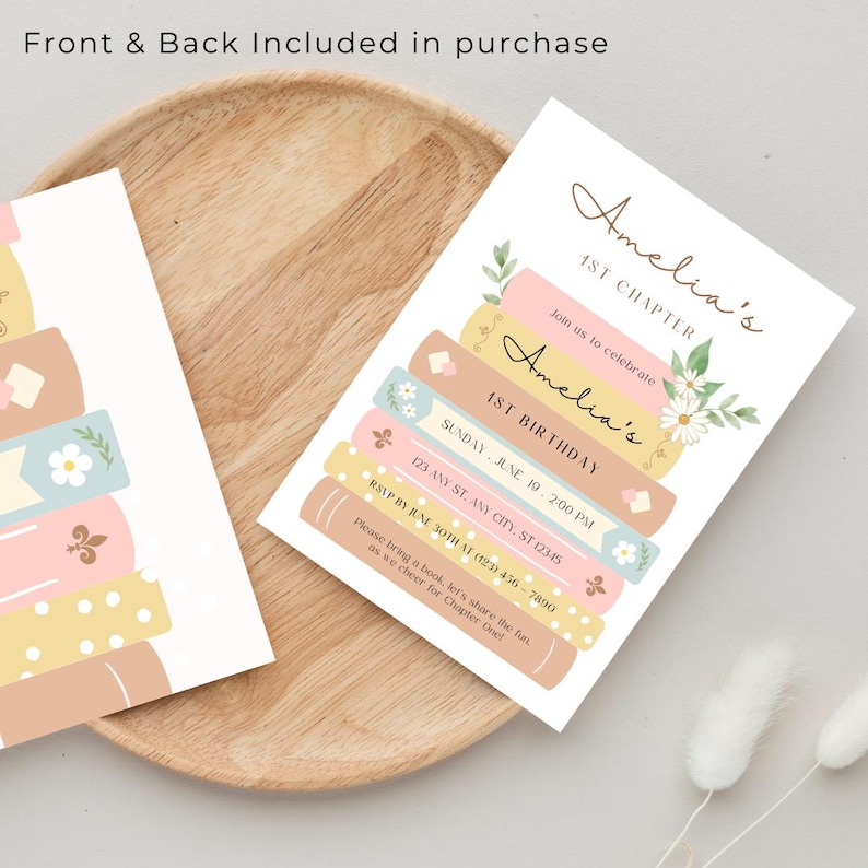 Op de afbeelding: Een afdrukbare uitnodiging voor een eerste verjaardagsfeest met een boekthema. De uitnodiging toont een stapel kleurrijke boeken met bloemen en de tekst "Amelia's 1st Chapter" en "Amelia's 1st Birthday".