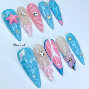 Puede incluir: Un conjunto de diez u&ntilde;as postizas largas y puntiagudas con varios dise&ntilde;os. Los dise&ntilde;os incluyen un remolino rosa y blanco, un remolino azul y blanco, una flor rosa y blanca, una concha azul y blanca, una estrella de mar azul y blanca y un dise&ntilde;o de burbujas azul y blanco. Las u&ntilde;as est&aacute;n pintadas con un acabado brillante.