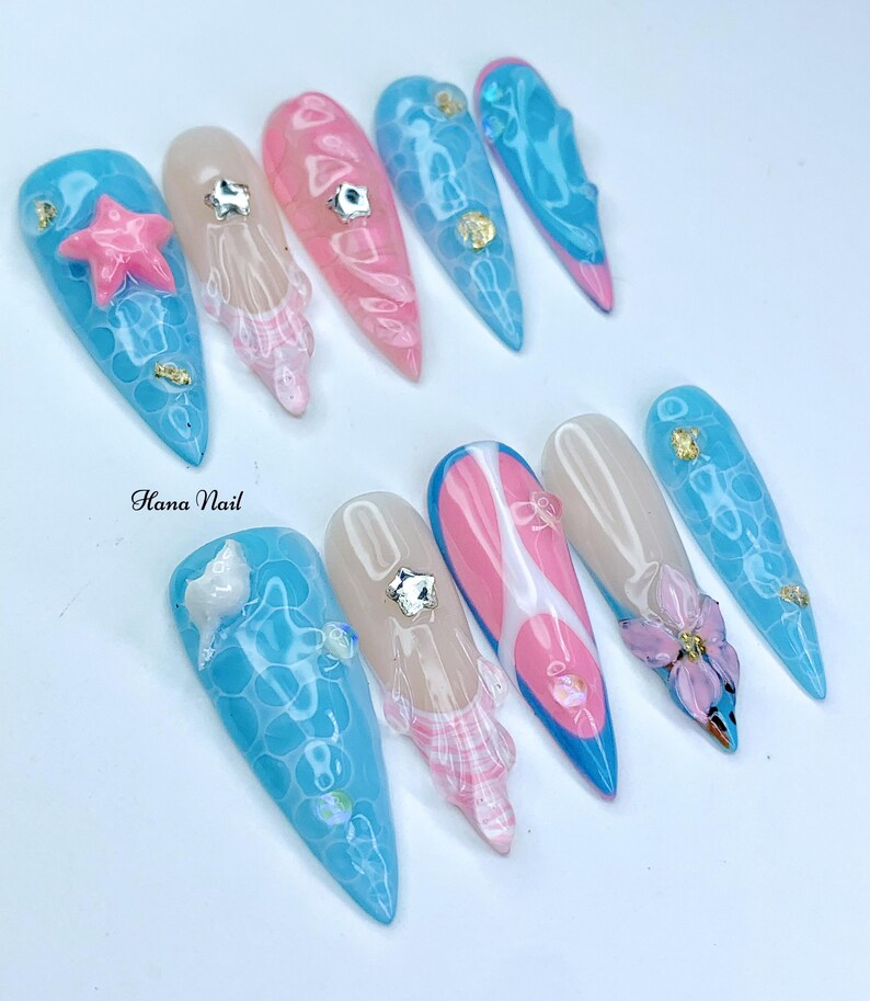 Puede incluir: Un conjunto de diez u&ntilde;as postizas largas y puntiagudas con varios dise&ntilde;os. Los dise&ntilde;os incluyen un remolino rosa y blanco, un remolino azul y blanco, una flor rosa y blanca, una concha azul y blanca, una estrella de mar azul y blanca y un dise&ntilde;o de burbujas azul y blanco. Las u&ntilde;as est&aacute;n pintadas con un acabado brillante.