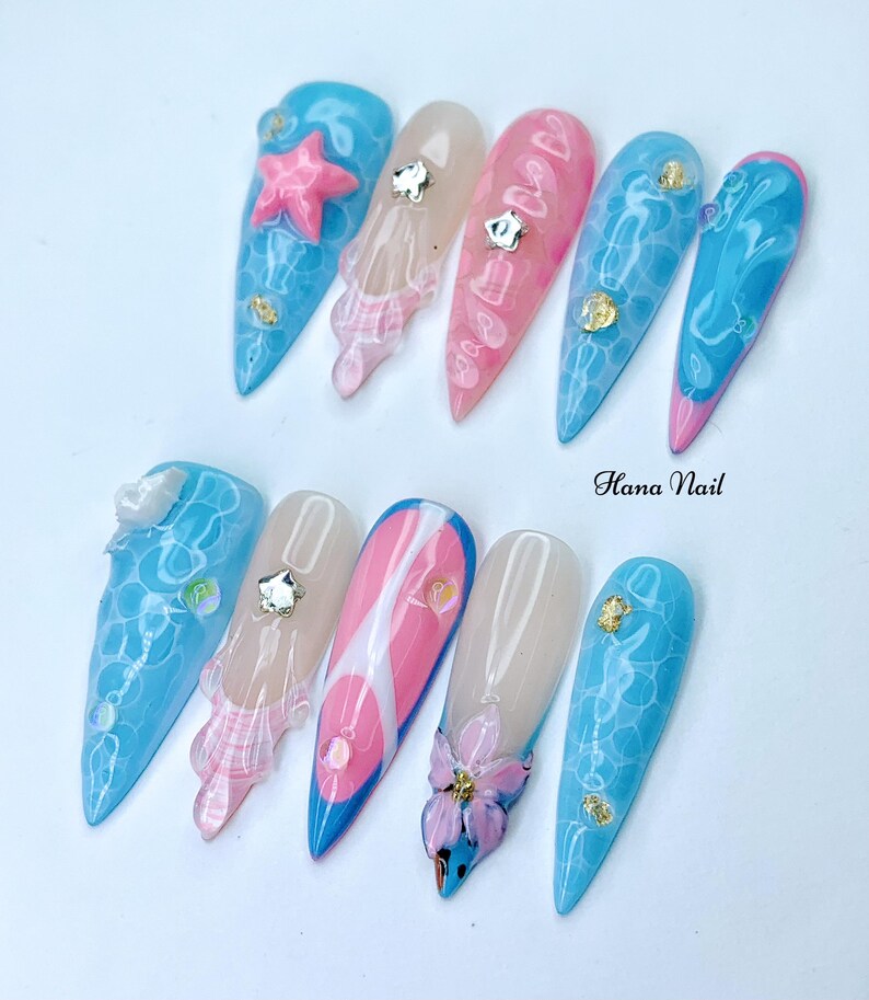 Puede incluir: Un conjunto de diez u&ntilde;as postizas largas y puntiagudas con varios dise&ntilde;os. Algunas u&ntilde;as est&aacute;n pintadas con una base azul claro y tienen un dise&ntilde;o de remolino blanco, mientras que otras est&aacute;n pintadas con una base rosa claro y tienen un dise&ntilde;o de remolino blanco. Algunas u&ntilde;as tienen un dise&ntilde;o 3D, como una estrella de mar, una flor o una concha. Las u&ntilde;as est&aacute;n dispuestas en dos filas sobre un fondo blanco. El texto "Hana Nail" es visible en la imagen.