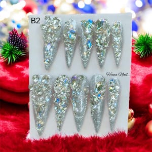 May include: A set of ten silver stiletto false nails with a silver glitter finish and rhinestones. The nails are arranged on a white card with the text "B2" and "Hana Nail" printed on it.